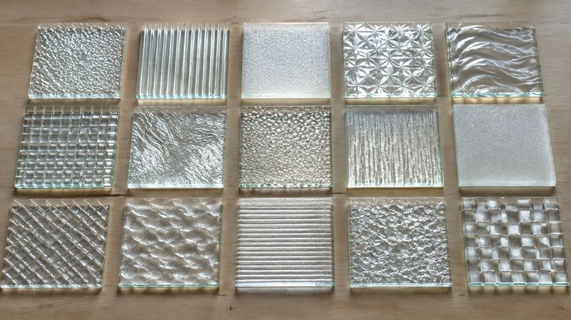 Obscure and patterned glass sample squares laid out and backlit so the textures read clearly